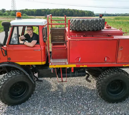 Man sieht einen roten Unimog 416 als Feuerwehrfahrzeug und Stephan Klotz sitzt am Steuer.