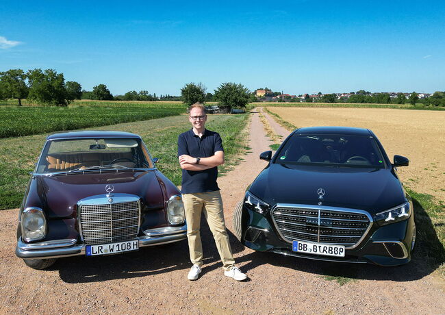 Man sieht Stephan Klotz, wie er zwischen seinem Mercedes-Benz W108 und einer modernen S-Klasse des Typs W223 steht.