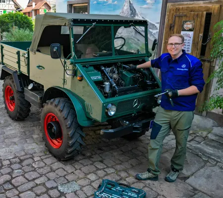 Man sieht Stephan Klotz in Arbeitskleidung mit Werkzeug an seinem Unimog 411 schrauben.